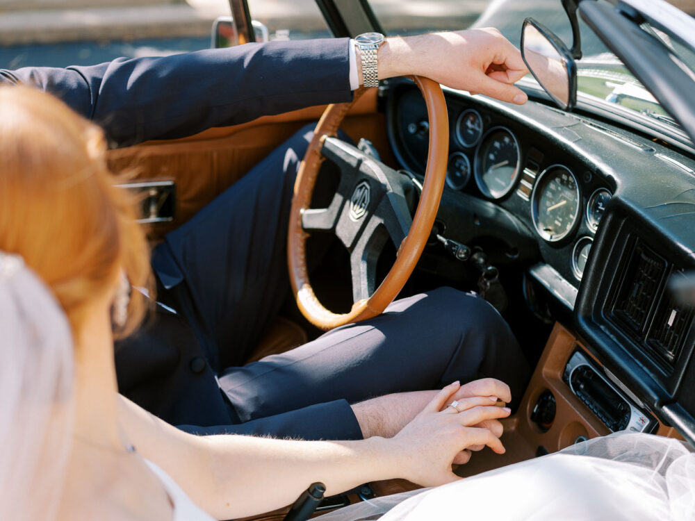 Bride and groom holding hands in a vintage car