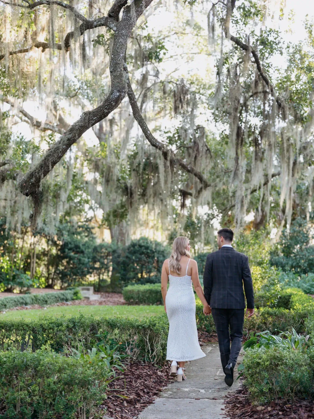 Bride and groom walking among moss covered trees during their engagement session in Charleston, SC
