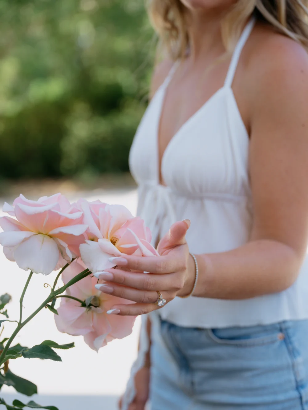 Bride touching a rose at Hampton Park in Charleston, showcasing her engagement ring